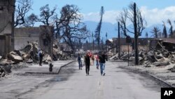 Unas personas caminan por una calle ante los daños causados por un incendio forestal, el viernes 11 de agosto de 2023, en Lahaina, Hawái.