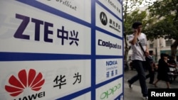 一名中國男子從武漢街頭有著華為和中興標誌的廣告牌前走過。（資料照片）