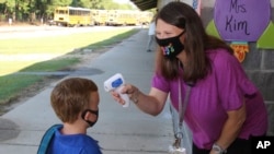 Asisten pengajar di Newton County Schools berbicara dengan siswa TK saat dia mengukur suhu tubuhnya di Decatur, Mississippi, Senin, 3 Agustus 2020. (Foto: AP)