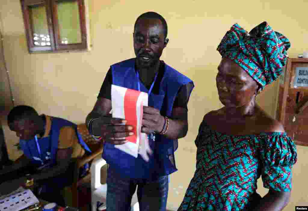 An election official shows to a woman how to cast her ballot during Liberia's presidential election in Monrovia, Oct. 10, 2017.