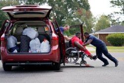 Lake Charles Fire Department personnel Alvin Taylor, right, and Jeremy Harris, left, assist Tim Williams into a transport van as he evacuates Lake Charles, La., Aug. 26, 2020, ahead of Hurricane Laura.