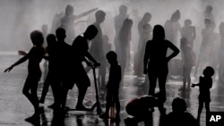 Children and adults cool off in a fountain in a park by the river in Madrid, Spain, June 12, 2022. 