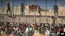 FILE - Riot police officers cordon off the area after migrants arrive on Spanish soil after crossing the fences separating the Spanish enclave of Melilla from Morocco in Melilla, Spain, June 24, 2022.