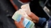 El asistente de un conductor de autobús cuenta un fajo de billetes de Bolívar en una parada de autobús frente a la estación de metro Antimano en Caracas, el 15 de marzo de 2021..