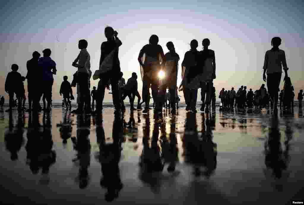 Siluet orang-orang terlihat saat mereka berjalan di sepanjang pantai Laut Arab di Mumbai, India. 