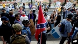 FILE - A white supremacist carries the Confederate flag as he walks past counterdemonstrators in Charlottesville, Va., Aug. 12, 2017.