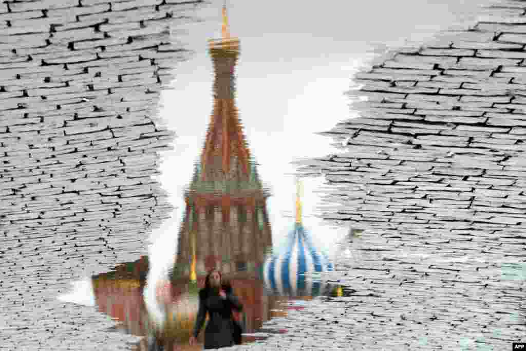 Foto ini, diputar 180 derajat, menunjukkan seorang perempuan yang tercermin dalam genangan air ketika ia berjalan melewati Katedral Saint Basil di Red Square di Moskow, Rusia.