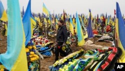A man carries flowers to lay at the grave of a killed soldier in a city cemetery in Kharkiv, Ukraine, March 21, 2023.