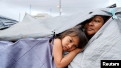 Las migrantes hondureñas Kami y su tía Mariana escuchan a otros migrantes discutir las normas de higiene dentro del campamento de migrante, en Tijuana, México, el 22 de abril de 2021.