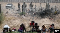 Migrants seeking asylum in the United States are watched by the Texas National Guard while they remain on the bank of the Rio Grande after having crossed from Ciudad Juarez, Chihuahua State, Mexico, on June 4, 2024. (Photo by HERIKA MARTINEZ / AFP)