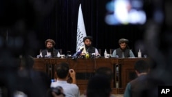 FILE - In front of a Taliban flag, Taliban spokesman and now the group's deputy culture and information Minister Zabihullah Mujahid, center, speaks at a news conference, in Kabul, Afghanistan, Aug. 17, 2021. 
