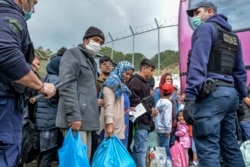 FILE - Migrants wait to board on buses outside Moria camp on their way to the port of Mytilene, on the northeastern Aegean island of Lesbos, Greece, May 3, 2020.