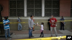 Un hombre le da un periódico a su nieta mientras espera para votar durante el segundo ensayo de votación en una escuela secundaria en Caracas, Venezuela. Noviembre 15, 2020.