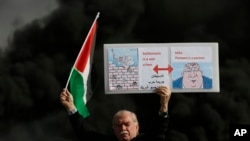 A Palestinian holds a poster depicting Israeli Prime Minister Benjamin Netanyahu, left, and U.S. Secretary of State Mike Pompeo as clashes with Israeli troops broke out at checkpoint Beit El near the West Bank city of Ramallah, Nov. 26, 2019.