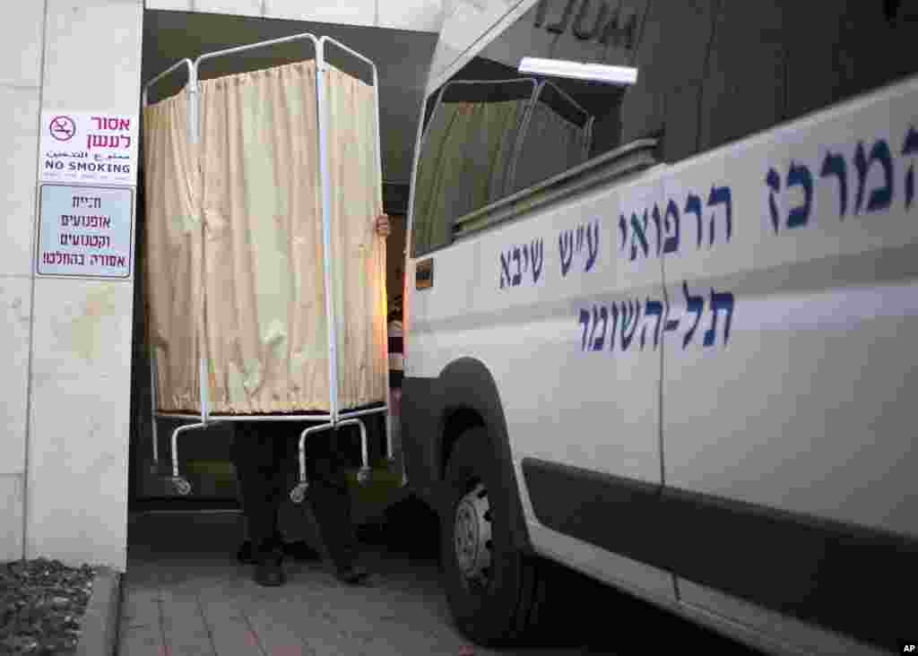 An Israeli policeman holds up a hospital curtain to block the view of the body of the late Prime Minister Ariel Sharon as it is transferred into an ambulance to be taken from the Sheba Medical Center near Tel Aviv, Israel, Jan. 11, 2014.