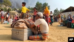 Rohingya refugees salvage their belongings and watch smoke rising following a fire at the Rohingya refugee camp in Balukhali, southern Bangladesh, March 22, 2021.