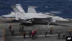 Un F-18 Super Hornet de la Marina de EEUU y miembros de la tripulación se ven en la cubierta de vuelo del USS Nimitz frente a la costa de Busan, Corea del Sur, el lunes 27 de marzo de 2023.