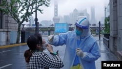 中国上海，一名穿戴防护装备的医务人员正为一名居民采集拭子样本，进行核酸测试（2022年4月26日）。