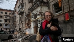 Seorang warga lokal tampak menggendong seekor kucing dan pergi meninggalkan gedung apartemen yang hancur akibat serangan misil Rusia, di Kharkiv, pada 2 Januari 2024. (Foto: Reuters/Sofiia Gatilova)
