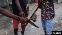 Integrantes de un grupo de vigilantes del vecindario sostienen un martillo y machetes mientras posan para una fotografía después de que el presunto líder de una pandilla, Makandal, fuera asesinado e incendiado, en Puerto Príncipe, Haití, el 20 de marzo de 2024.