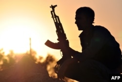 FILE - A fighter from the Kurdish People Protection Unit (YPG) poses for a photo at sunset in the Syrian town of Ain Issi, some 50 kilometers north of Raqqa, during clashes between IS group jihadists and YPG fighters on July 10, 2015.
