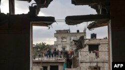 Fotografía tomada a través de la ventana de un edificio dañado por el bombardeo israelí muestra una familia de pie en un tejado, en Rafah, en el sur de la Franja de Gaza, el 27 de enero de 2024, mientras continúan los combates entre Israel y el grupo militante Hamás.