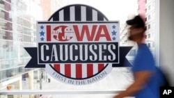ARCHIVO - Un peatón pasa junto a un cartel de los Caucus de Iowa en una pasarela elevada en el centro de Des Moines, Iowa, el 4 de febrero de 2020.