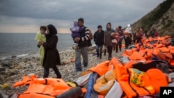FILE - Refugees and migrants walk along a beach after crossing part of the Aegean Sea on a dinghy, from Turkey to the Greek island of Lesbos, Dec. 12, 2015. 