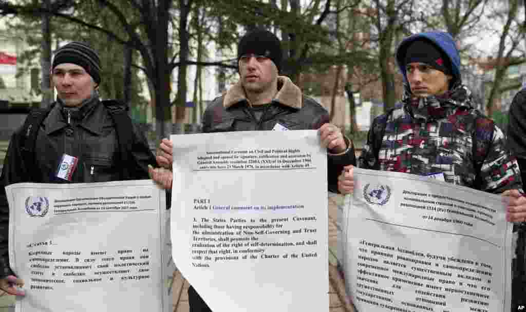 Demonstran pro-Rusia memegang cetakan dokumen PBB dalam ukuran besar tetang hak menentukan nasib bangsa sendiri di luar gedung parlemen regional di Simferopol, Krimea, Ukraina, 16 Maret 2014.