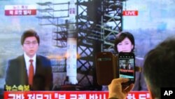 Seorang warga Korsel menggunakan telepon pintarnya untuk memotret siaran televisi yang memberitakan peluncuran roket Korea Utara di Stasiun Kereta Api di Seoul, Korsel (12/12). 