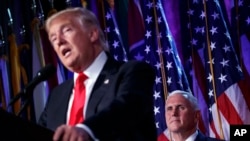 FILE - Vice president-elect Mike Pence, right, watches as President-elect Donald Trump speaks during an election night rally in New York, Nov. 9, 2016.