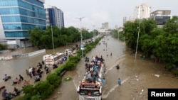 Sebagian warga duduk di atas atap bus, sementara lainnya berjalan melewati jalanan yang tergenang banjir di tengah pandemi Covid-19 di Karachi, Pakistan, 27 Agustus 2020.