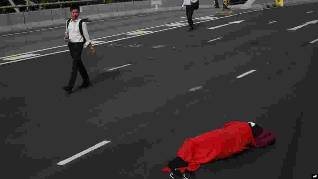 People walk to work as a protester sleeps on a main road in the occupied areas in Central district, Hong Kong, Oct. 9, 2014.