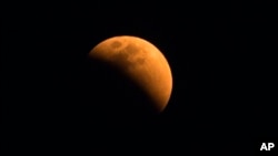 FILE - The moon turns a reddish hue as it passes through the earth's shadow during a lunar eclipse as seen in Gauhati, India, Jan. 31, 2018. 