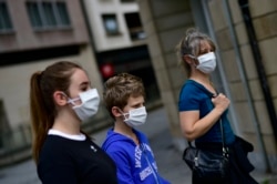 A family wearing face mask to protect of the coronavirus go for a walk, in Pamplona, northern Spain, Sunday, April 27, 2020. On Sunday, children under 14 years old will be allowed to take walks with a parent for up to one hour.