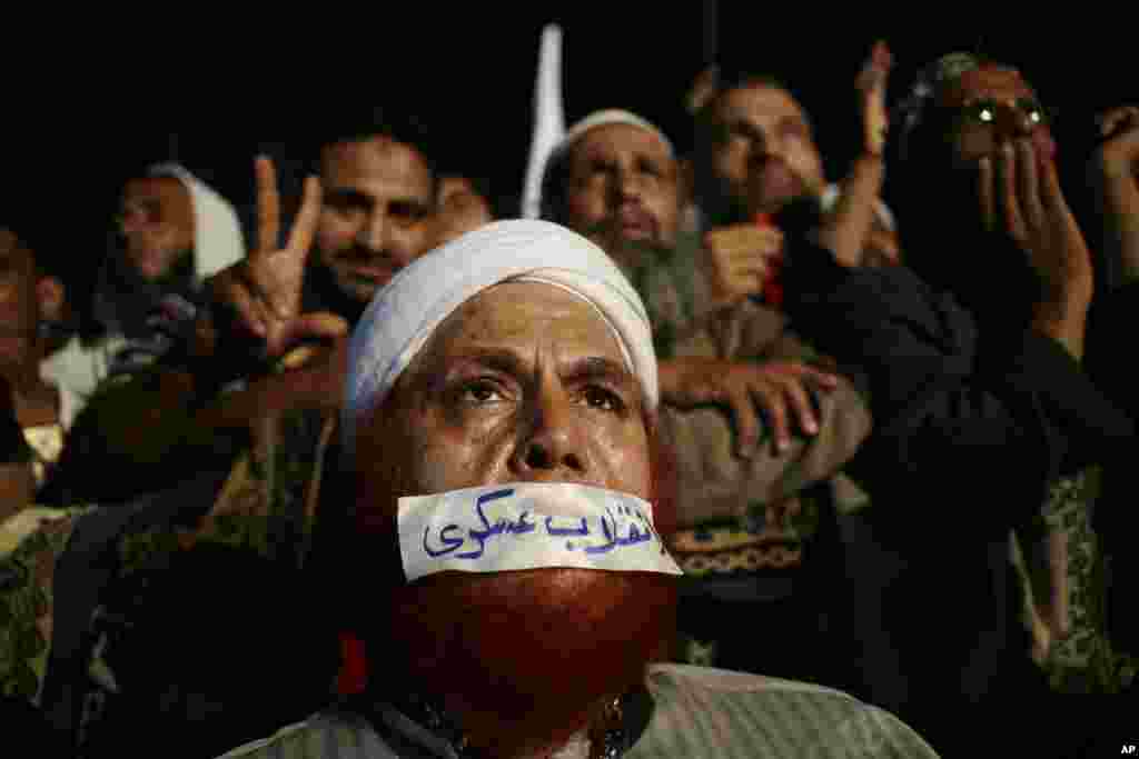 A supporter of Egypt's ousted President Mohamed Morsi gets relief from the afternoon heat with the help of water sprayers in front of a poster of Morsi, Cairo University,Giza, Egypt.