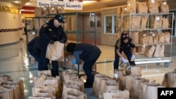 FILE - Bagged meals to be distributed to children are prepared to be delivered by volunteers and members of the Alexandria Sheriff's Office at the closed T.C. Williams high school in Alexandria, Virginia, March 16, 2020.