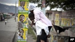 Man, carrying woman with cholera symptoms, walks past campaign posters showing presidential candidate Jude Celestin in Port-au-Prince, Haiti, 11 Nov., 2010.