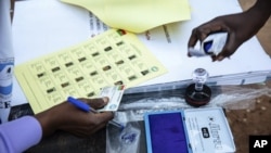 Election officials check identification papers of people who lined up to vote in Burkina Faso's presidential and legislative elections, as polling stations open in Ouagadougou, Nov. 22, 2020.