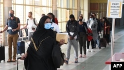 FILE - Travelers wearing masks walk at Jomo Kenyatta International Airport in Nairobi, Aug. 1, 2020. Kenyan officials have raised suspicions over the deaths of 89 Kenyans, most of them domestic workers, in Saudi Arabia.