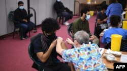 FILE - Members of the public receive a dose of the AstraZeneca/Oxford vaccine at a coronavirus vaccination center at the Fazl Mosque in southwest London, March 23, 2021.