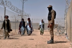 FILE - In this Aug. 20, 2021, file photo, Pakistani army soldier stands guard while Afghan people enter into Pakistan through a border crossing point, in Chaman, Pakistan.