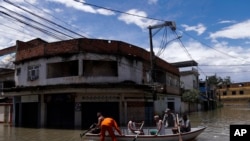 Los bomberos evacuan a los residentes a través de una calle inundada después de una lluvia mortal en Belford Roxo, Brasil, el lunes 15 de enero de 2024.