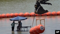 Trabajadores toman un descanso de colocar boyas para que sean utilizadas como barrera fronteriza en el río Bravo, el miércoles 12 de julio de 2023, a la altura de Eagle Pass, Texas. (AP Foto/Eric Gay)