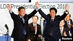 日本首相安倍晋三（右）在东京自民党总部再次当选该党领袖后与前国防部长石破茂举起双手。 （2018年9月20日）