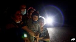 FILE - In this May 17, 2021, file photo a group of migrants mainly from Honduras and Nicaragua wait along a road after turning themselves in upon crossing the U.S.-Mexico border, in La Joya, Texas.