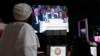 Members of the media watch Syrian National Coalition (SNC) President Mouaz al-Khatib during a live address during the opening of the Arab League summit in Doha, March 26, 2013.