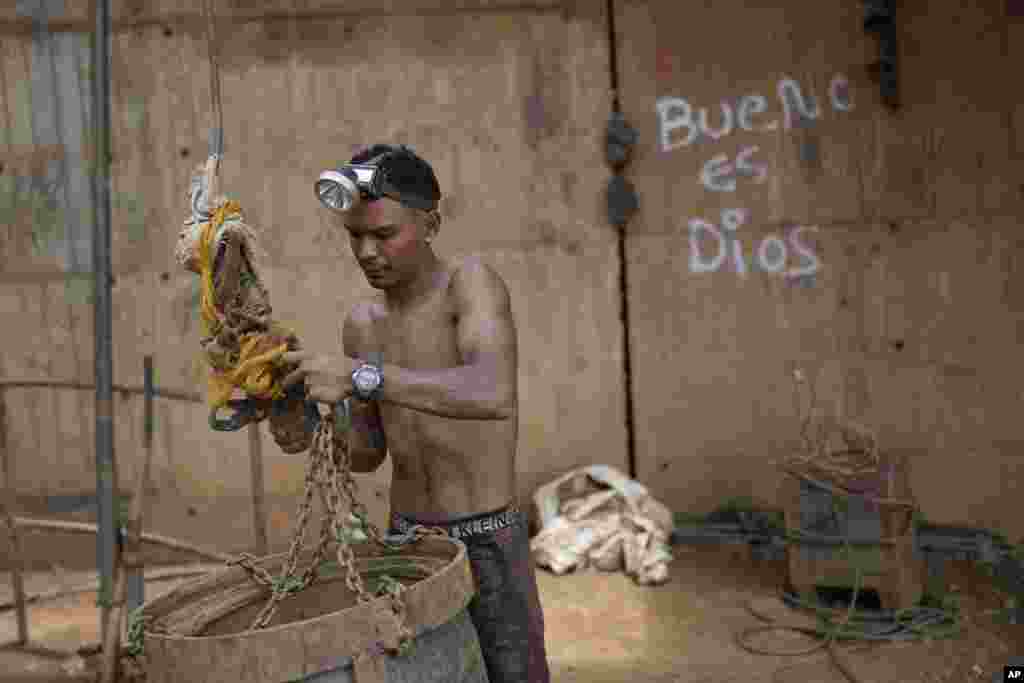 Un trabajador sujeta un gran cubo a un sistema de poleas para subir piedras por un pozo en una mina subterránea de oro en El Callao, estado Bolívar, en Venezuela, el viernes 28 de abril de 2023. Los cubos también son utilizados para subir y bajar herramientas en el lugar. 