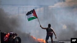 Un manifestante ondea la bandera palestina durante los enfrentamientos con las fuerzas israelíes en el puesto de control de Hawara, al sur de la ciudad cisjordana de Naplusa, el viernes 14 de mayo de 2021.