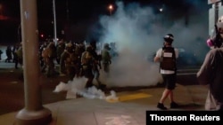 A member of the media stands amid tear gas used by police officers to clear protesters near an Immigration and Customs Enforcement centre in Portland 20 Aug 2020.